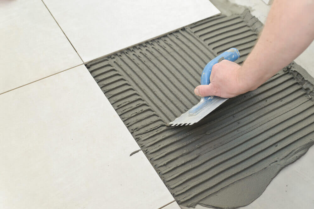 Close up of a tiler putting down the ground and ready to lay down the floor tiles