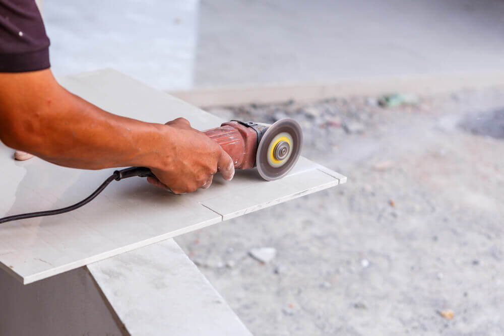Image of a tiler Mandurah worker cutting a small rectangle off the end of a large whit tile with an angle grinder