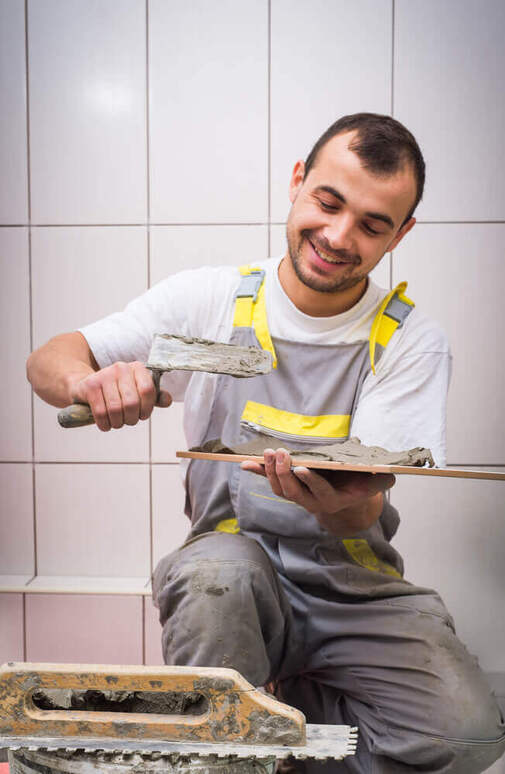A tiler Mandurah worker kneeling down whilst putting on some grout on the back of a tile in his arms