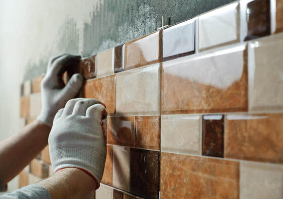 A tiler Mandurah worker wearing gloves whilst laying on some wall tiles that are shades of brown