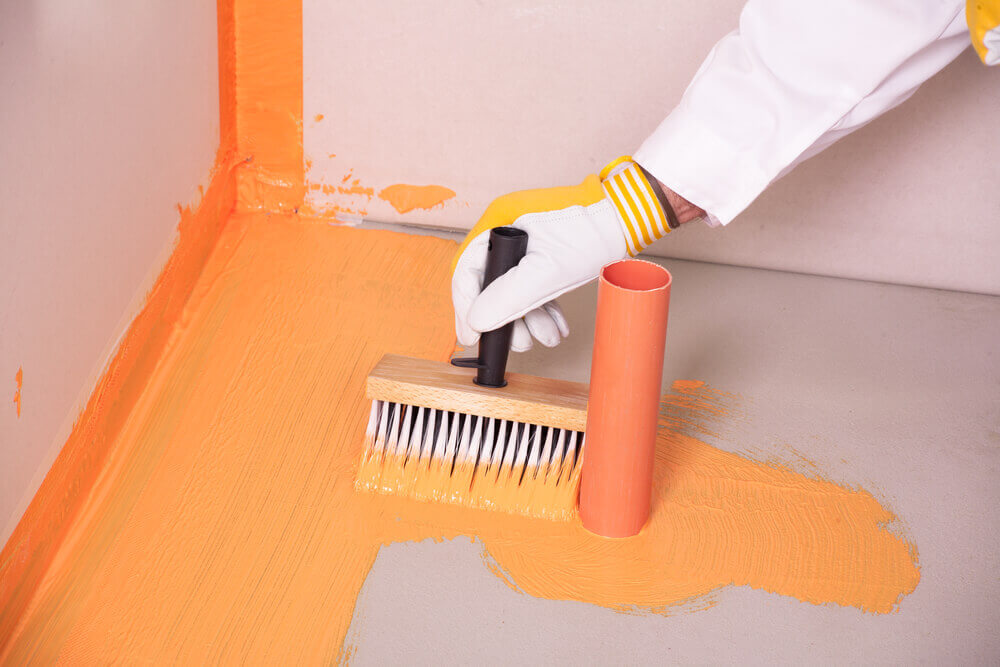 A tiler Mandurah worker painting on waterproofing paint on a bathroom floor wearing a white glove